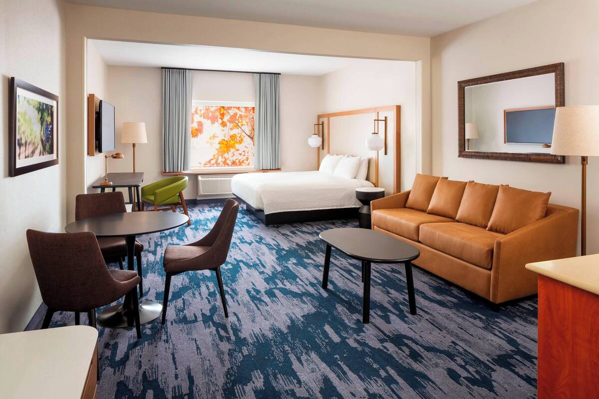 Habitación de hotel con cama, sofá, escritorio con silla, una mesita y televisor.