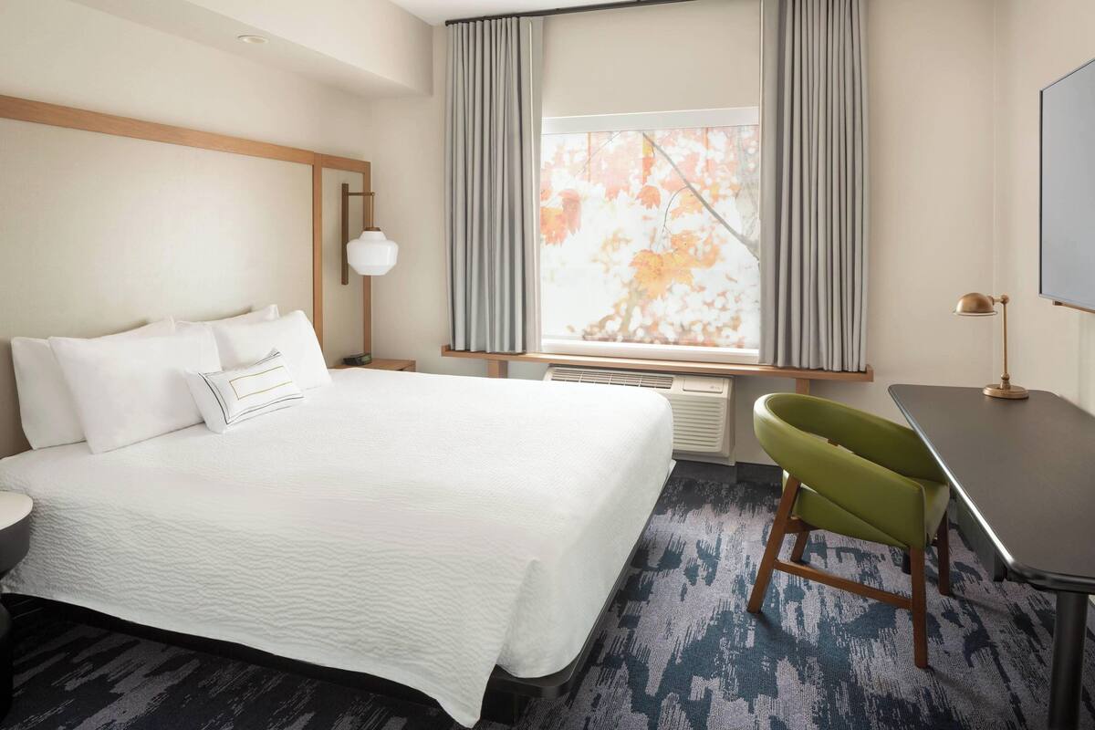 Una habitación de hotel con una cama grande, un escritorio, una silla y una ventana con cortinas.