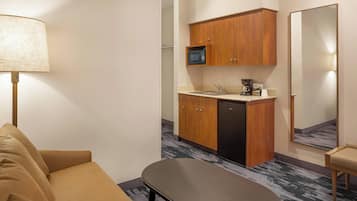 Une chambre d’hôtel compacte comprenant un canapé, une petite table, une kitchenette avec un four à micro-ondes, une machine à café et un miroir.