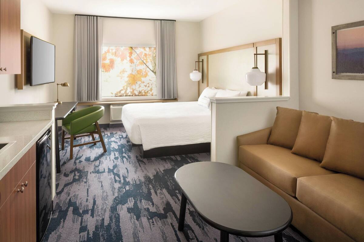 Habitación de hotel con cama, sofá, escritorio con silla, televisor y ventana con cortinas.