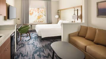 Habitación de hotel con cama, sofá, escritorio con silla, televisor y ventana con cortinas.