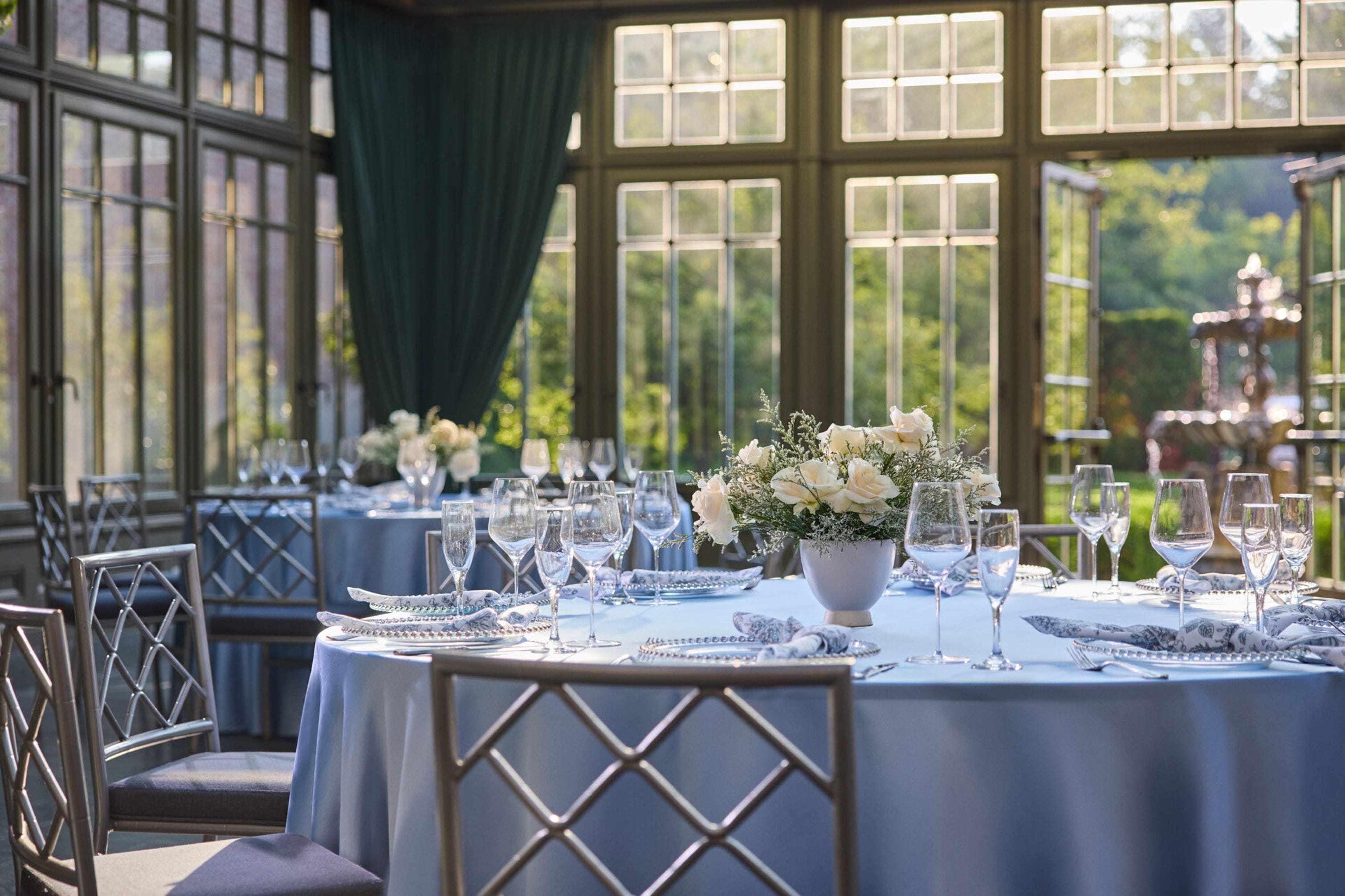 A dining area with round tables set for a meal, featuring white tablecloths and floral centerpieces.