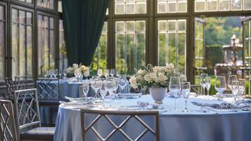 A dining area with round tables set for a meal, featuring white tablecloths and floral centerpieces.