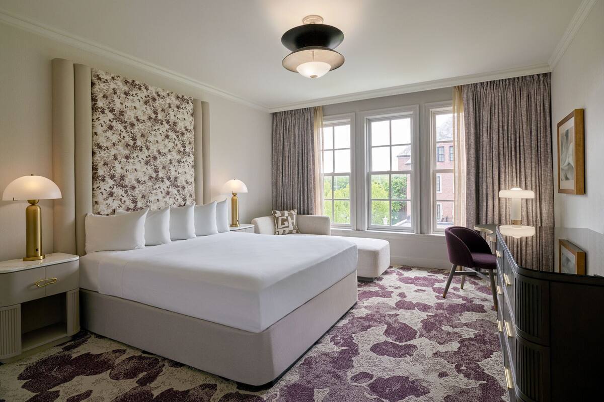 A spacious bedroom with a large bed, two bedside tables with lamps, a desk, and a chair.