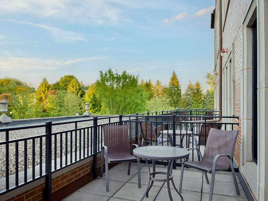 Een balkon met buitenmeubilair, een bakstenen muur en uitzicht op bomen en groen.