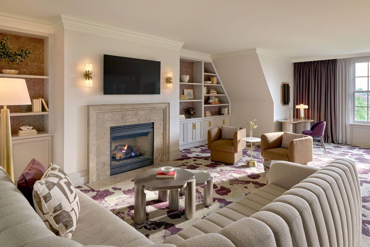 A modern living room with a fireplace, comfortable seating, a bookshelf, and a large window.