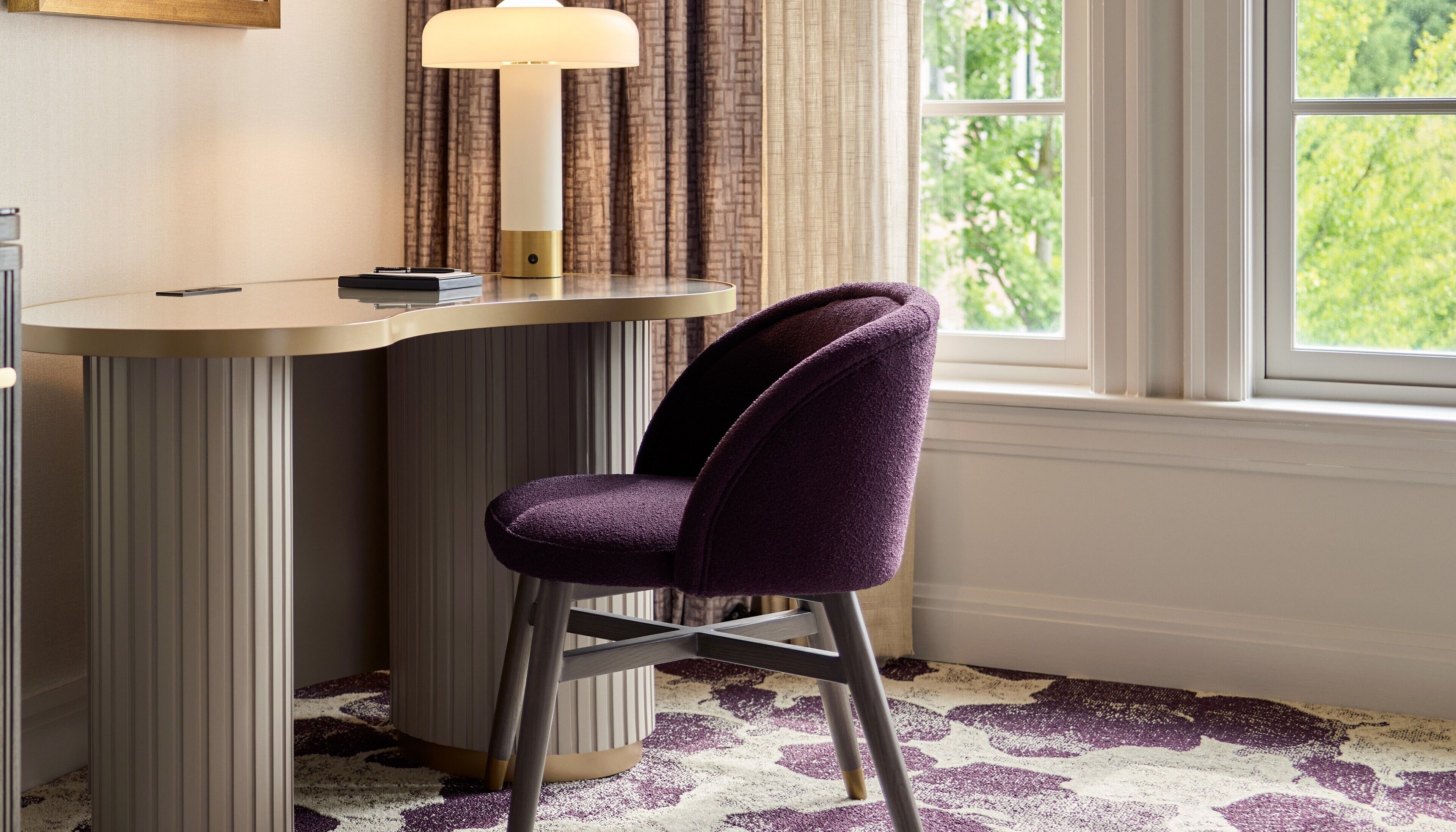 A corner desk with a lamp, a purple chair, and a patterned carpet.