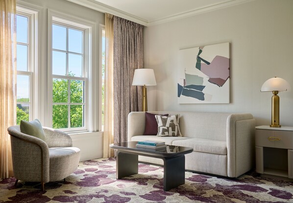 A living room with a sofa, armchair, coffee table, lamps, and artwork.