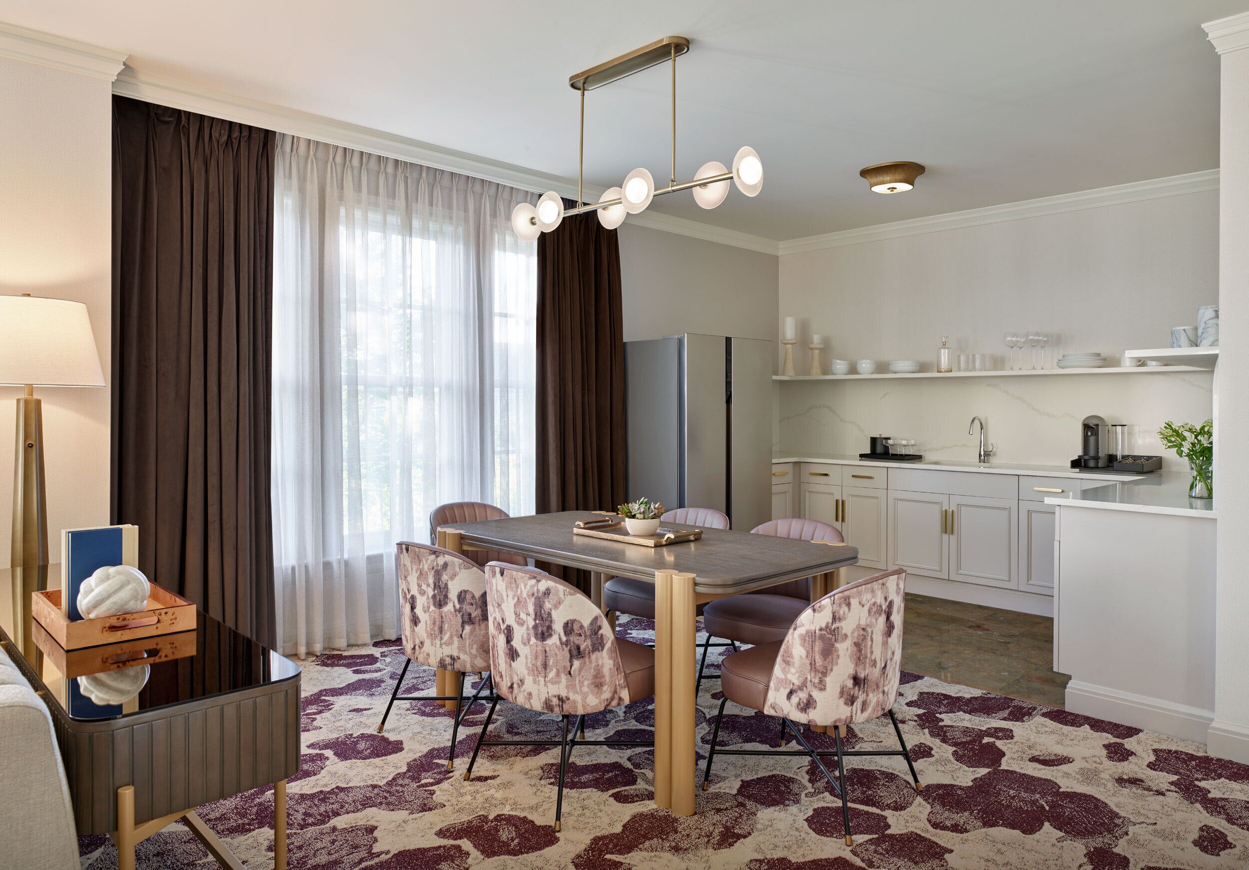Una habitación de hotel moderna con zona de comedor, cocina y un amplio ventanal con cortinas.