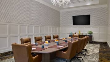 A conference room with a long table, brown leather chairs, a chandelier, a flat-screen TV, and a patterned wall.