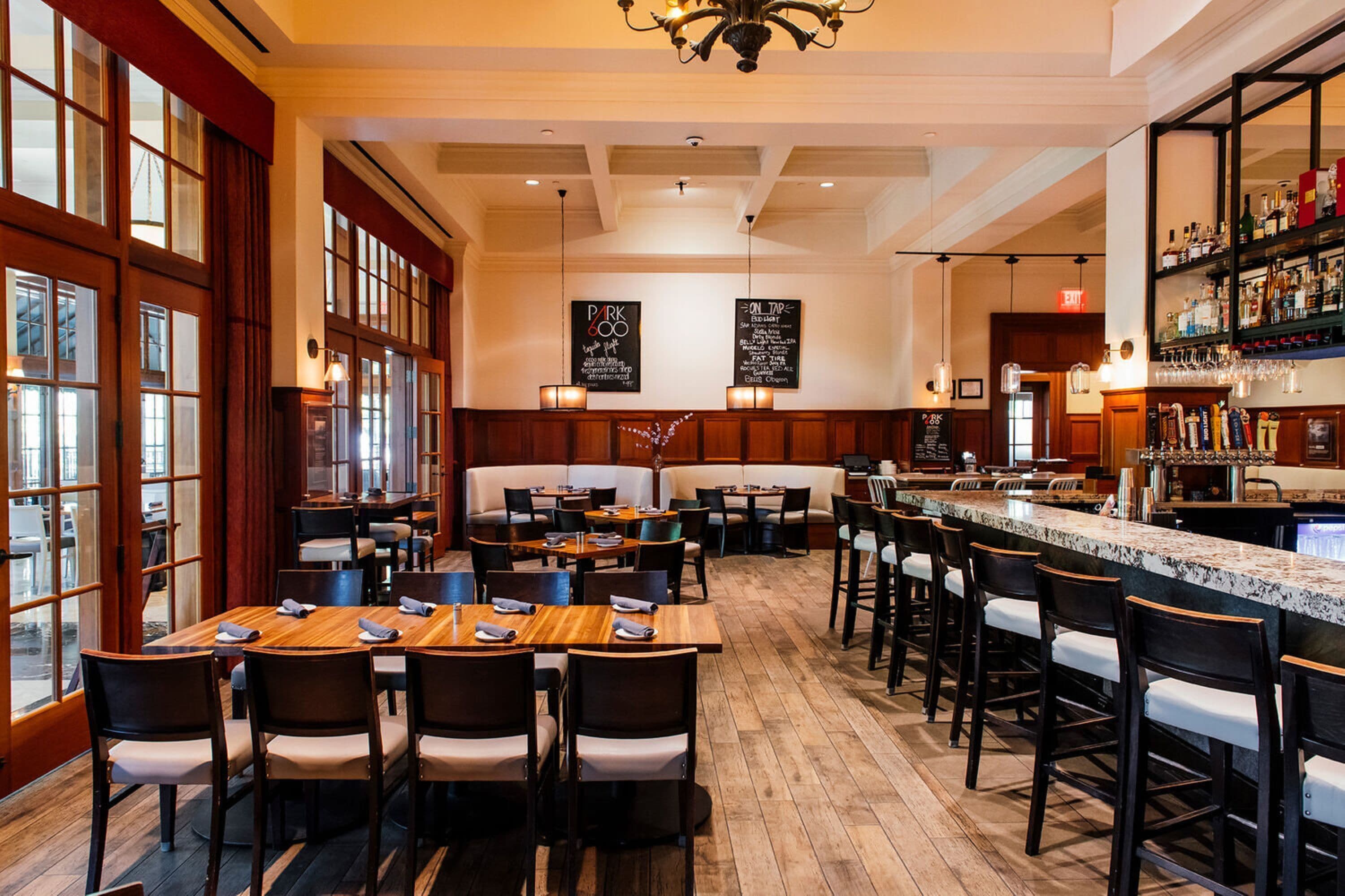 A restaurant with wooden tables and chairs, a bar area, and a menu board.