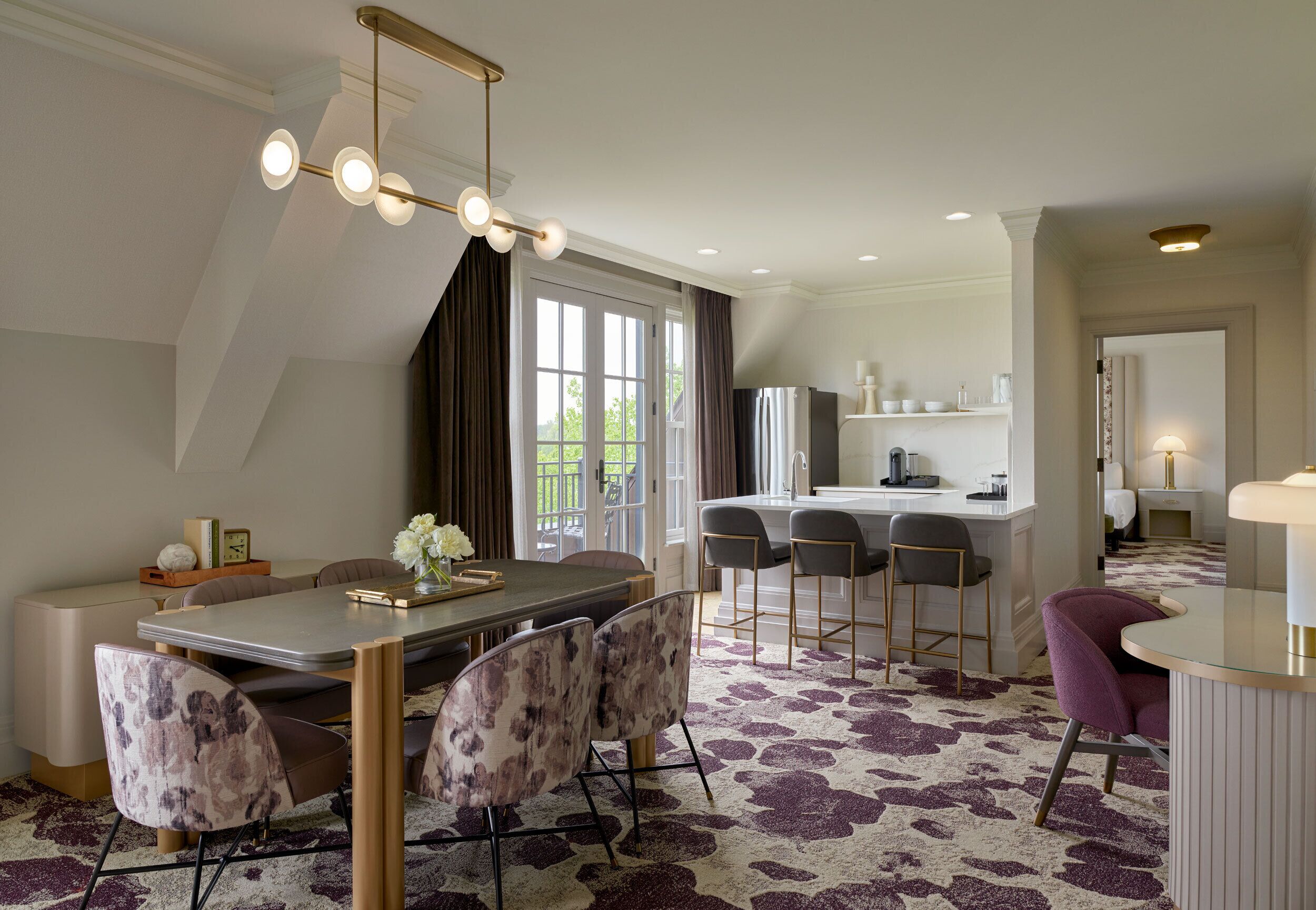 A modern dining area with a central table, bar stools, and a patterned carpet.