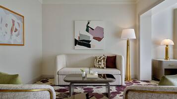 Una sala de estar moderna con un sofá, dos sillones, una mesita de centro y una lámpara de pie. Hay un cuadro en la pared y una pequeña mesa con libros y una planta.