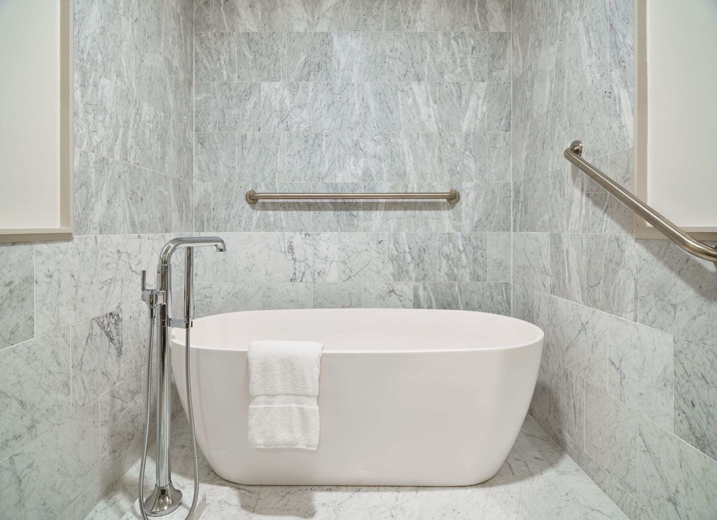 Un baño moderno con una bañera independiente, paredes de mármol y un asidero.