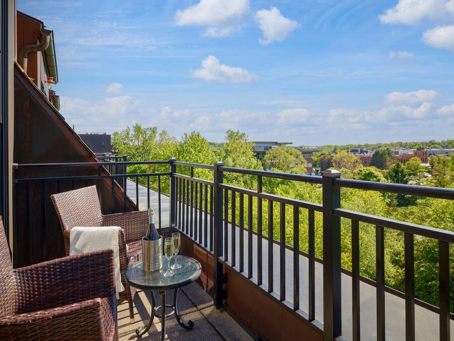 A balcony with wicker furniture, a glass table, and a bottle of champagne.