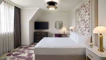 A hotel room with a large bed, a desk with a lamp, a flat-screen TV, and a decorative wall panel.