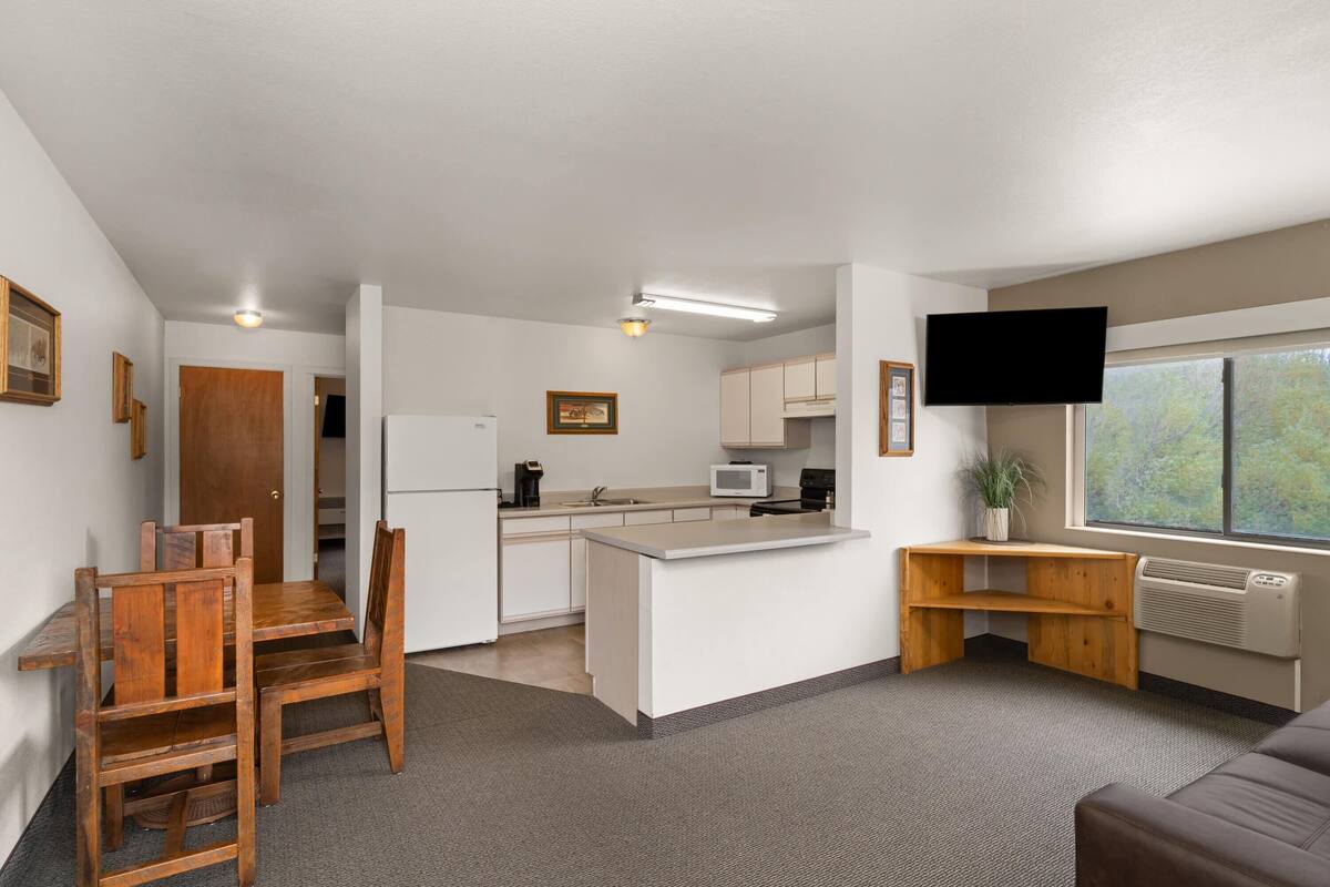 A compact living space with a kitchenette, a dining area, a seating area, and a TV mounted on the wall.