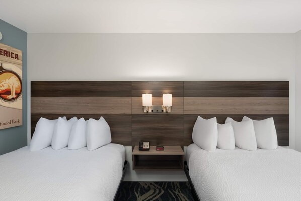 A hotel room with two beds, a wooden headboard, bedside lamps, a nightstand, and a wall decoration.