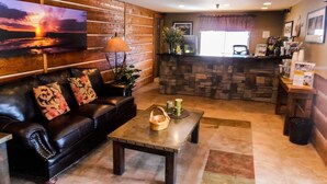 A living room with a black leather sofa, a coffee table, and a painting of a sunset.