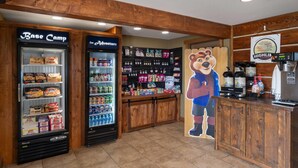 A food court with two refrigerated display cases labeled 'Base Camp' and 'For Adventure,' and a wooden counter with a coffee machine.