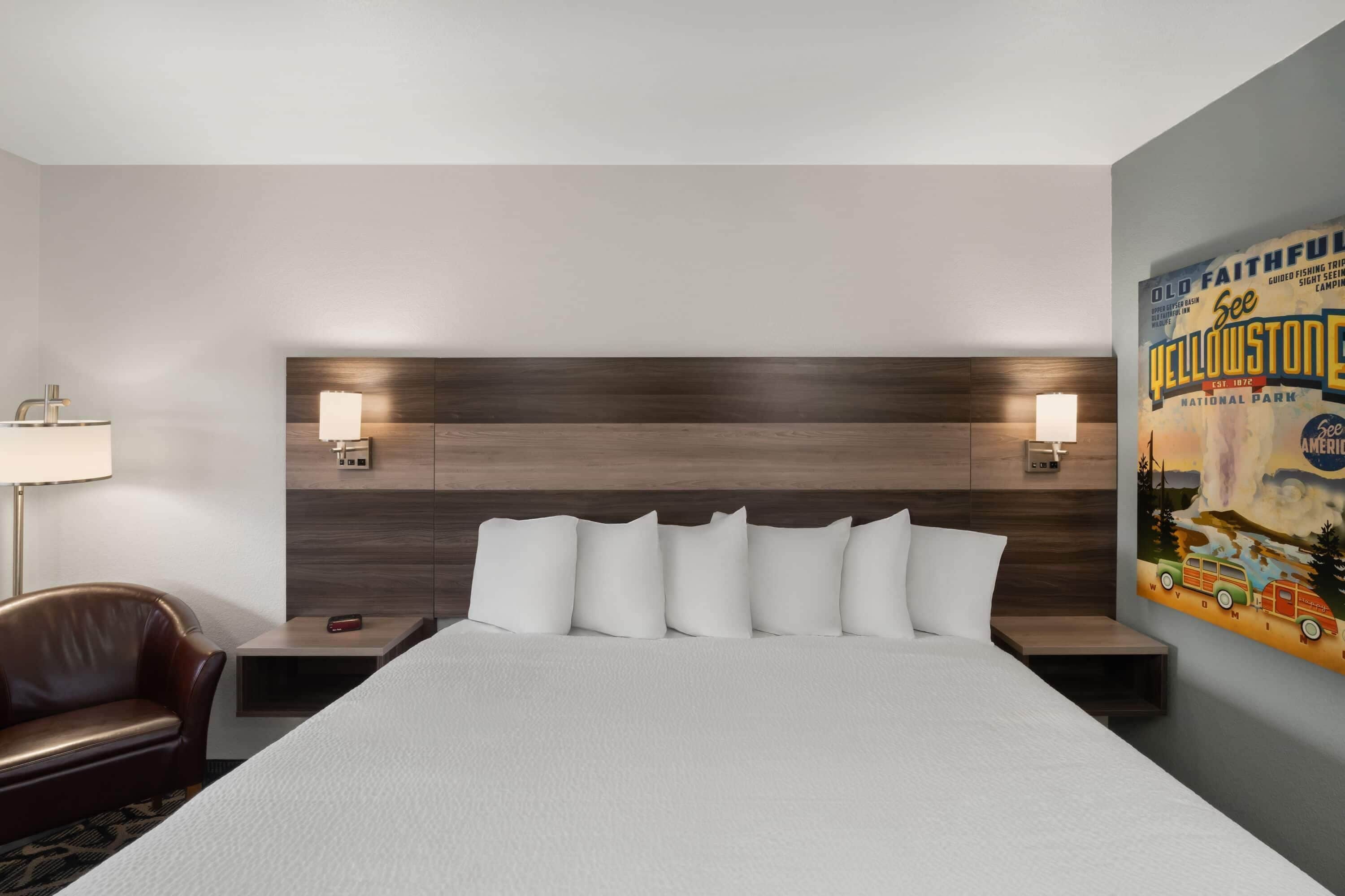 A hotel room with a large bed, two bedside tables, a nightstand, a lamp, a leather chair, and a wall poster.