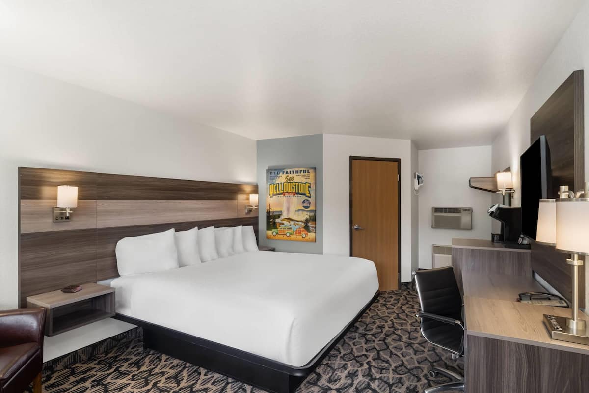 A hotel room with a bed, desk, chair, and a poster on the wall.