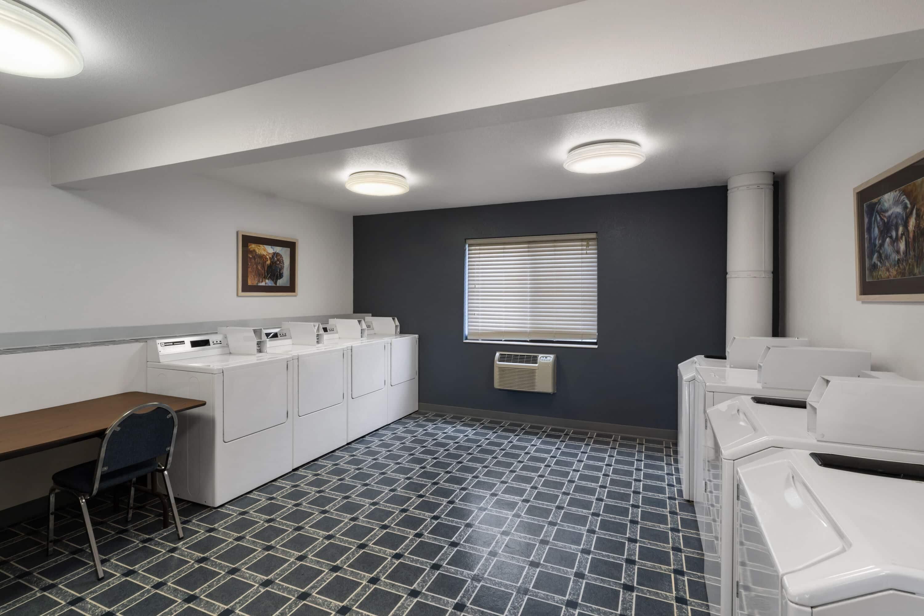 A laundry room with a desk, chairs, and a washing machine.