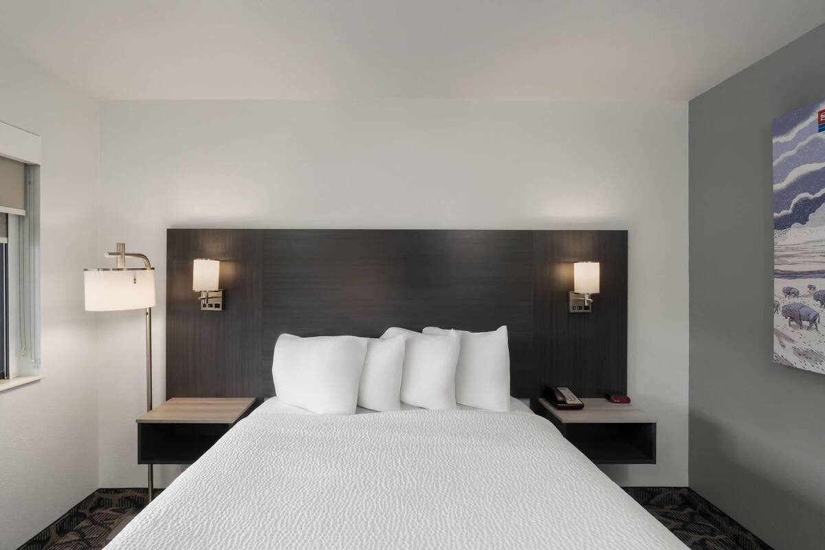 A hotel room with a large bed, bedside lamps, a nightstand, and a painting on the wall.