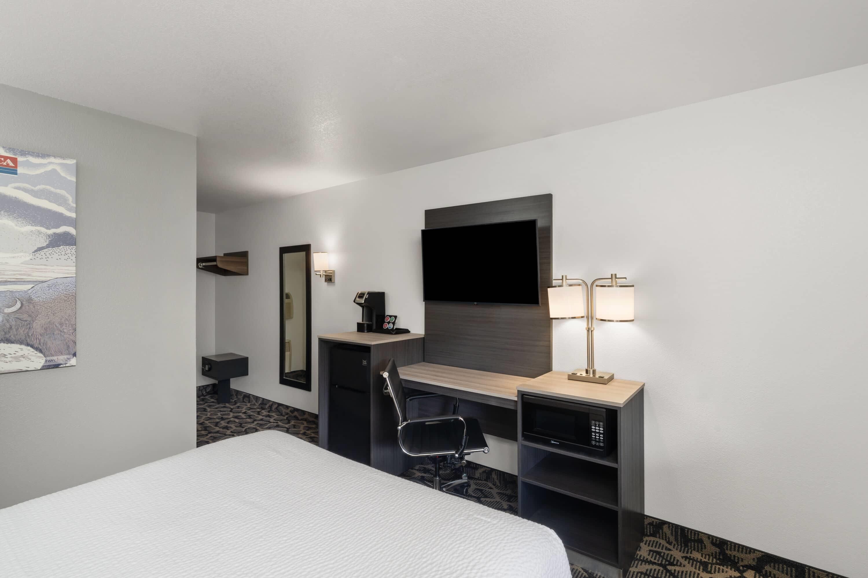 A hotel room with a bed, desk, chair, TV, and a lamp.
