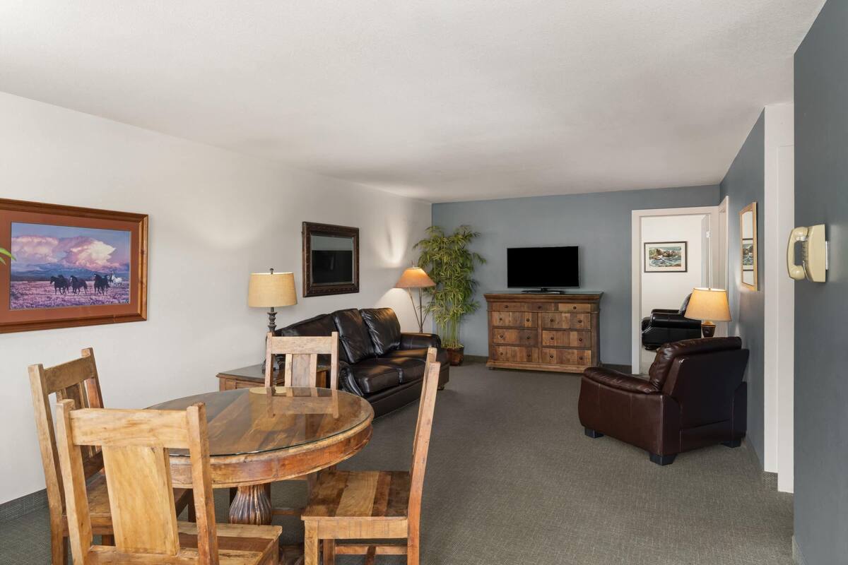 A living room with a round wooden table, two leather sofas, a TV, and a cabinet.