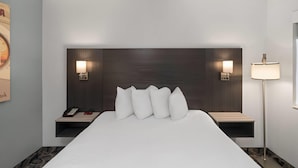 A hotel room with a large bed, bedside lamps, a nightstand with a phone, and a wall-mounted shelf.