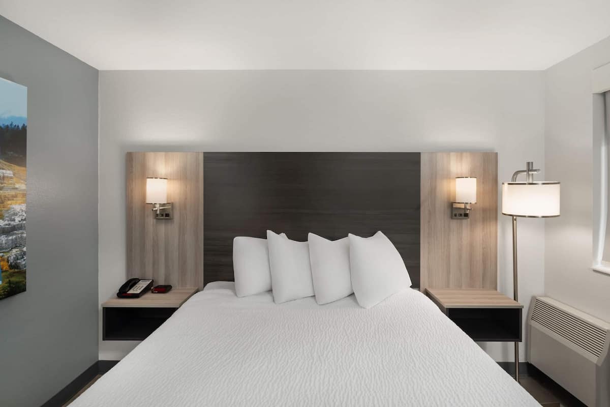 A modern hotel room with a large bed, bedside lamps, a phone, and a view of a mountainous landscape.