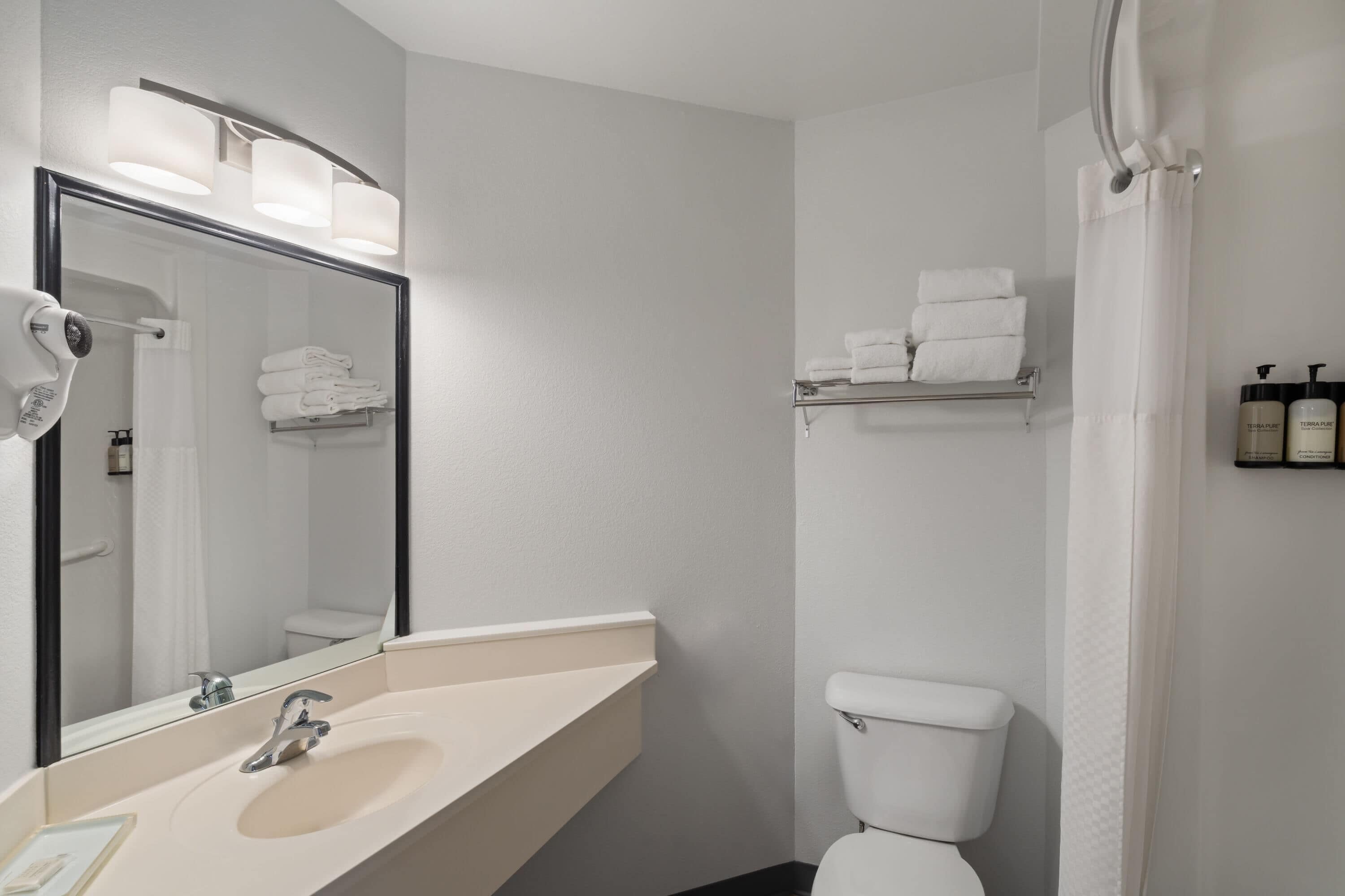 A bathroom with a sink, mirror, towel rack, toilet, and shower curtain.