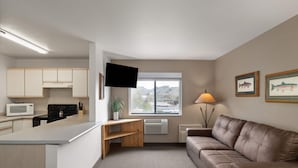 A modern kitchen with a flat-screen TV, a dining area with a sofa, and a window with a mountain view.