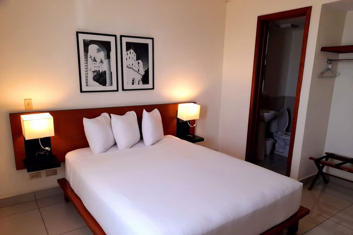 A hotel room with a large bed, two bedside lamps, a wooden headboard, and two framed pictures on the wall.
