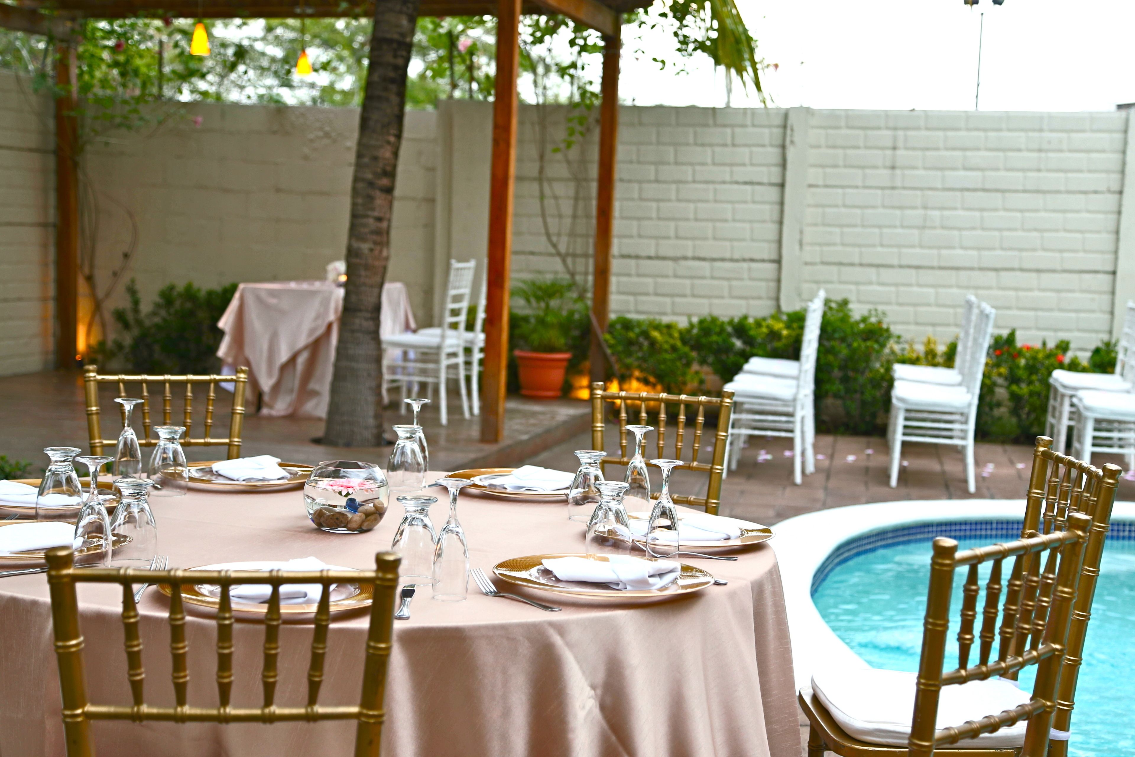 An outdoor dining area with round tables, gold chairs, and a pool.
