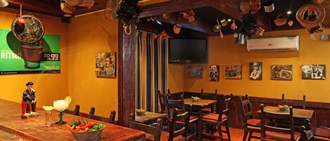 A restaurant with wooden tables and chairs, a TV mounted on the wall, and various decorations hanging from the ceiling.