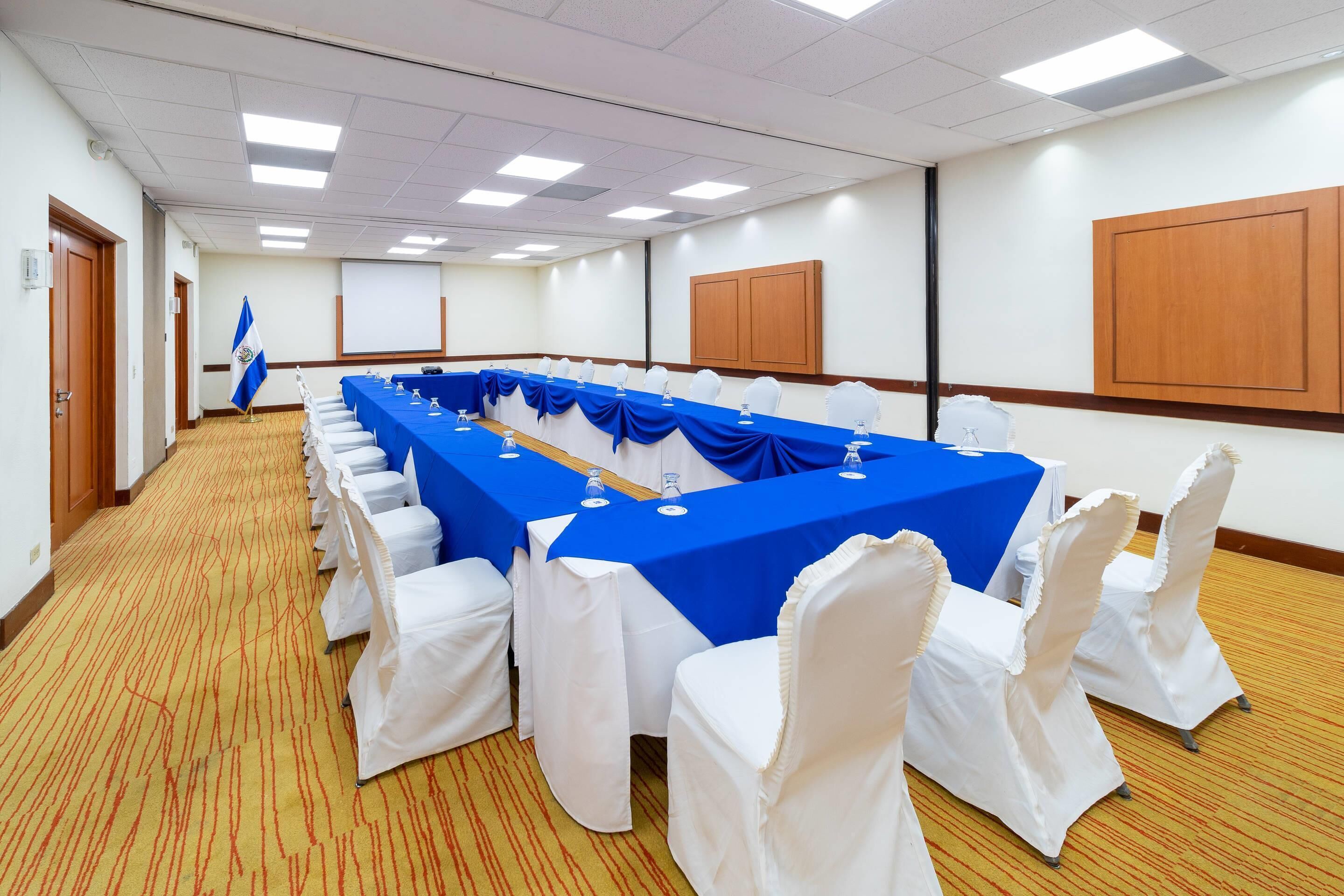A conference room with a long table, white chairs, and a blue tablecloth.