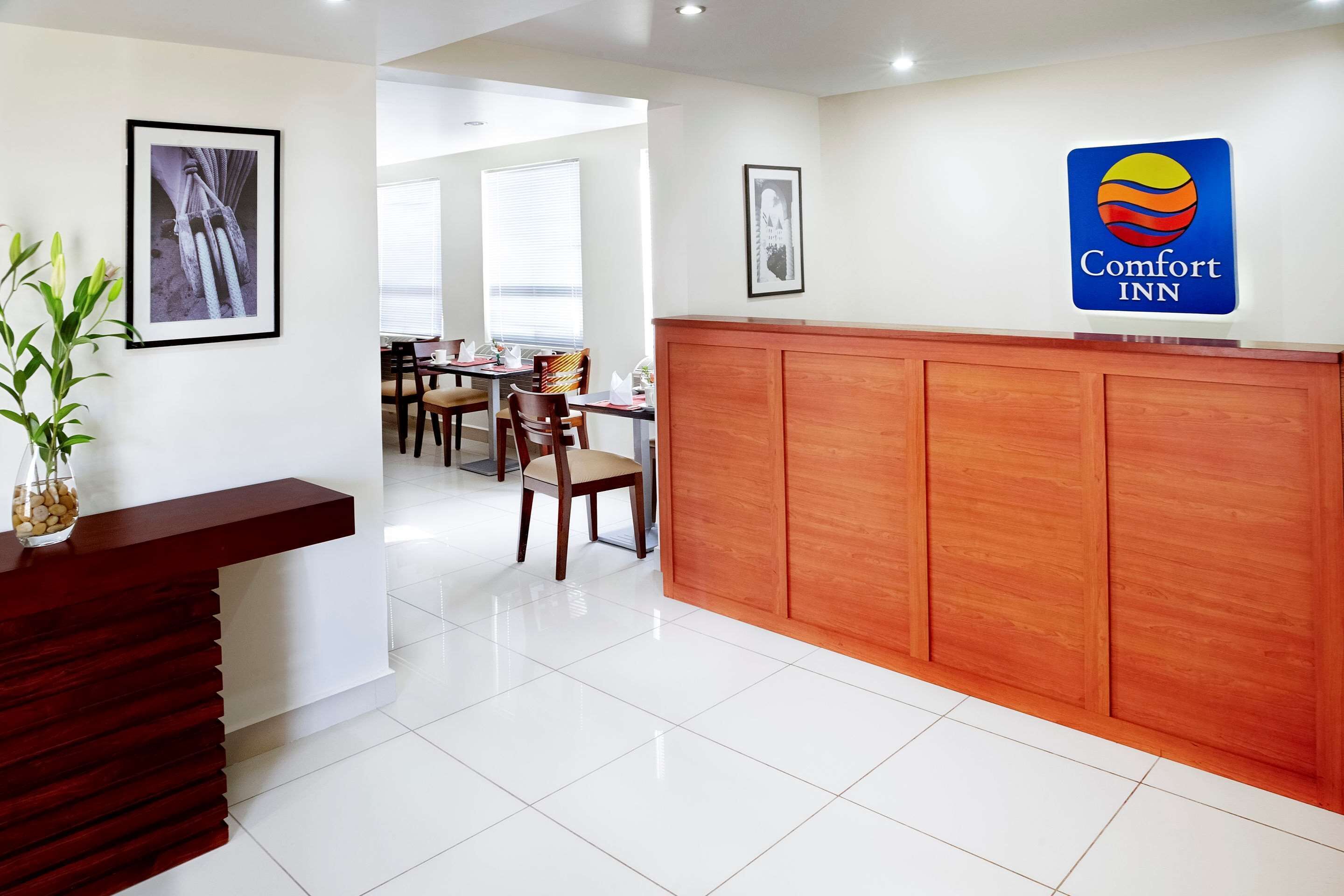 A hotel reception area with a wooden reception desk, framed artwork on the walls, and a Comfort Inn sign.