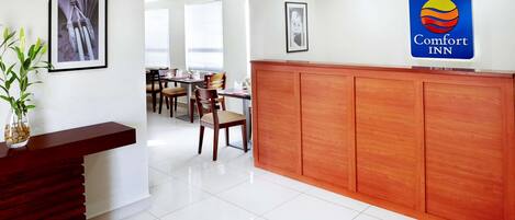 A hotel reception area with a wooden reception desk, framed artwork on the walls, and a Comfort Inn sign.