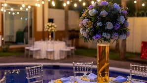 Un área de comedor al aire libre con mesas redondas, sillas y un arreglo floral decorativo en un jarrón alto.