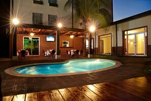 A pool area with a brick patio, outdoor seating, and a building with a TV screen and a bar area. - Comfort Inn Real San Miguel (San Miguel)