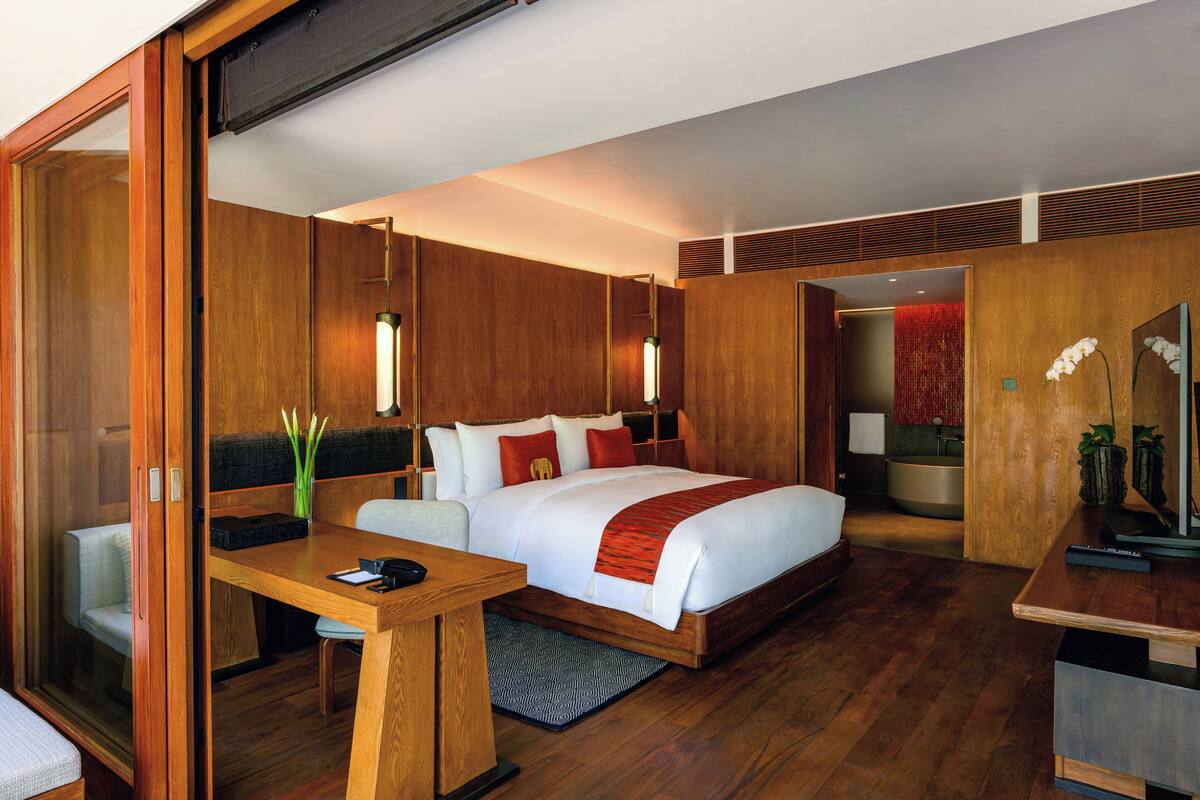 A modern bedroom with a large bed, wooden walls, and a desk with a chair.