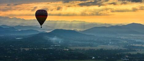 A hot air balloon flying over a landscape with mountains and fields.