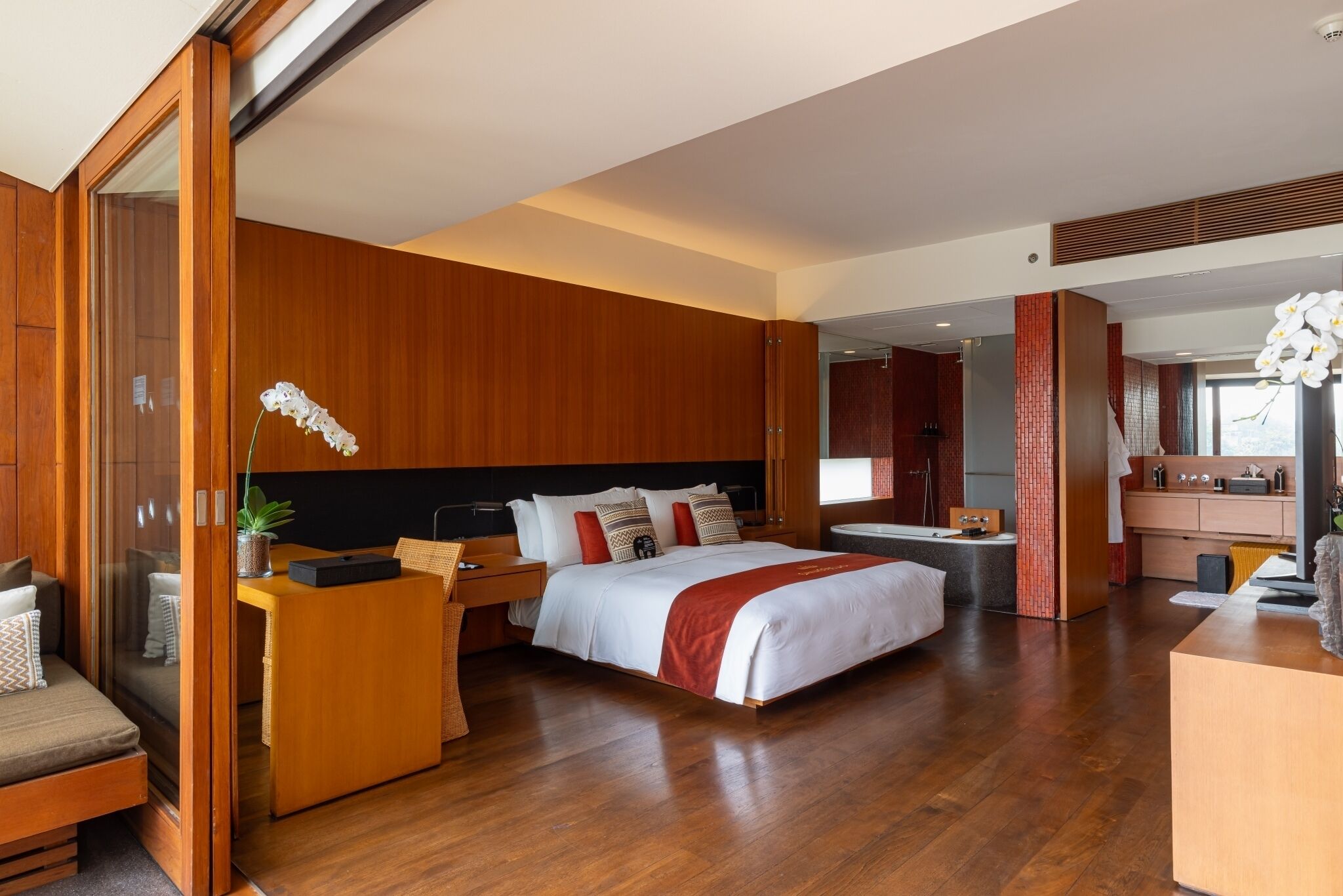 Una habitación de hotel moderna con una cama grande, suelo de madera, un escritorio y un baño visible a través de una puerta abierta.