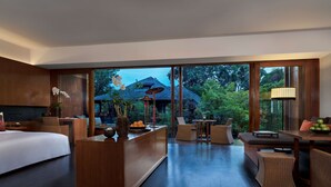 Une chambre d’hôtel moderne dotée d’un grand lit, d’un bureau en bois, de meubles en osier et offrant une vue sur une maison à travers de grandes fenêtres.