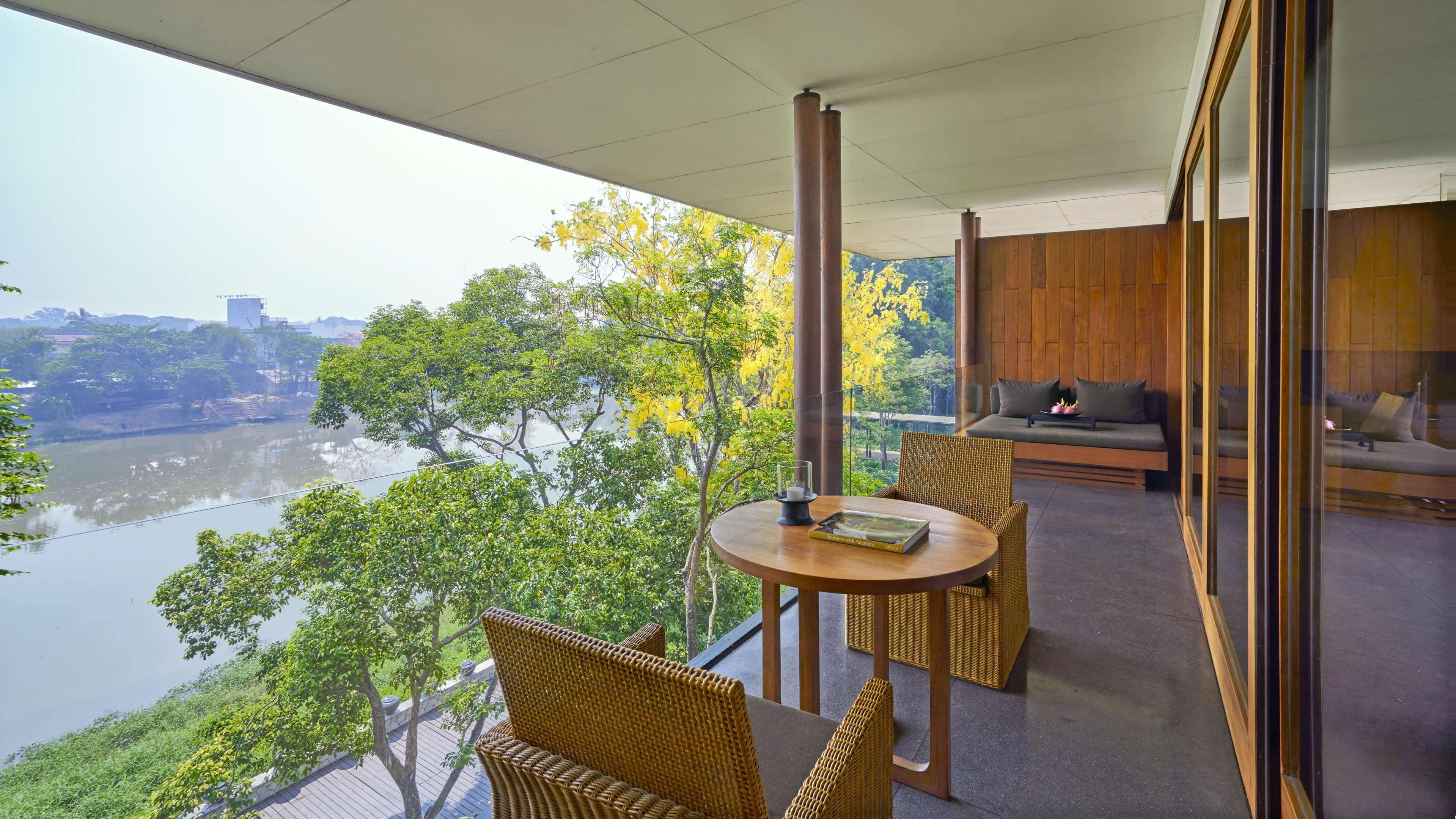 A balcony with wicker furniture, a table with a book, and a view of a river and trees.