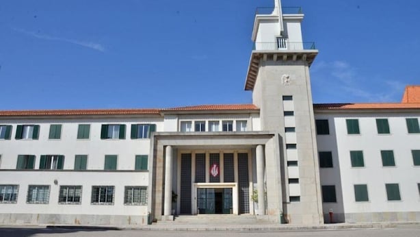 Un edificio con una torre destacada que presenta una cruz, una entrada principal con un emblema decorativo y una serie de ventanas.