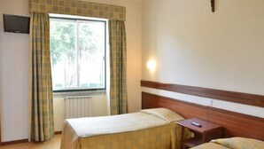 Una habitación con dos camas, una ventana con cortinas, un televisor de pared y una cruz en la pared.