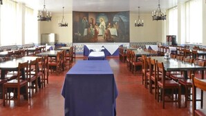 Un amplio comedor con numerosas mesas y sillas, un mural central y candelabros.
